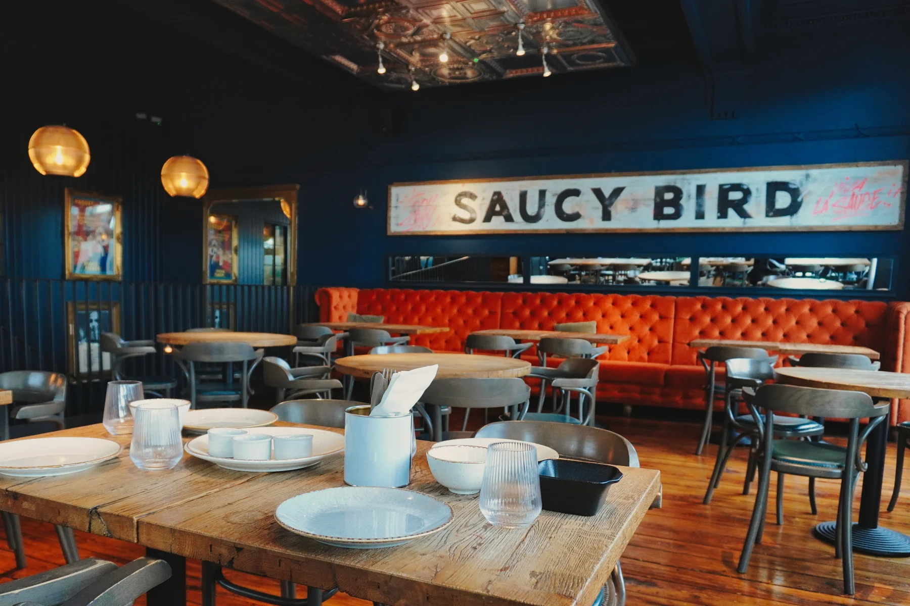 Saucy Bird dining room with orange banquette seating, set wooden tables and the Saucy Bird sign