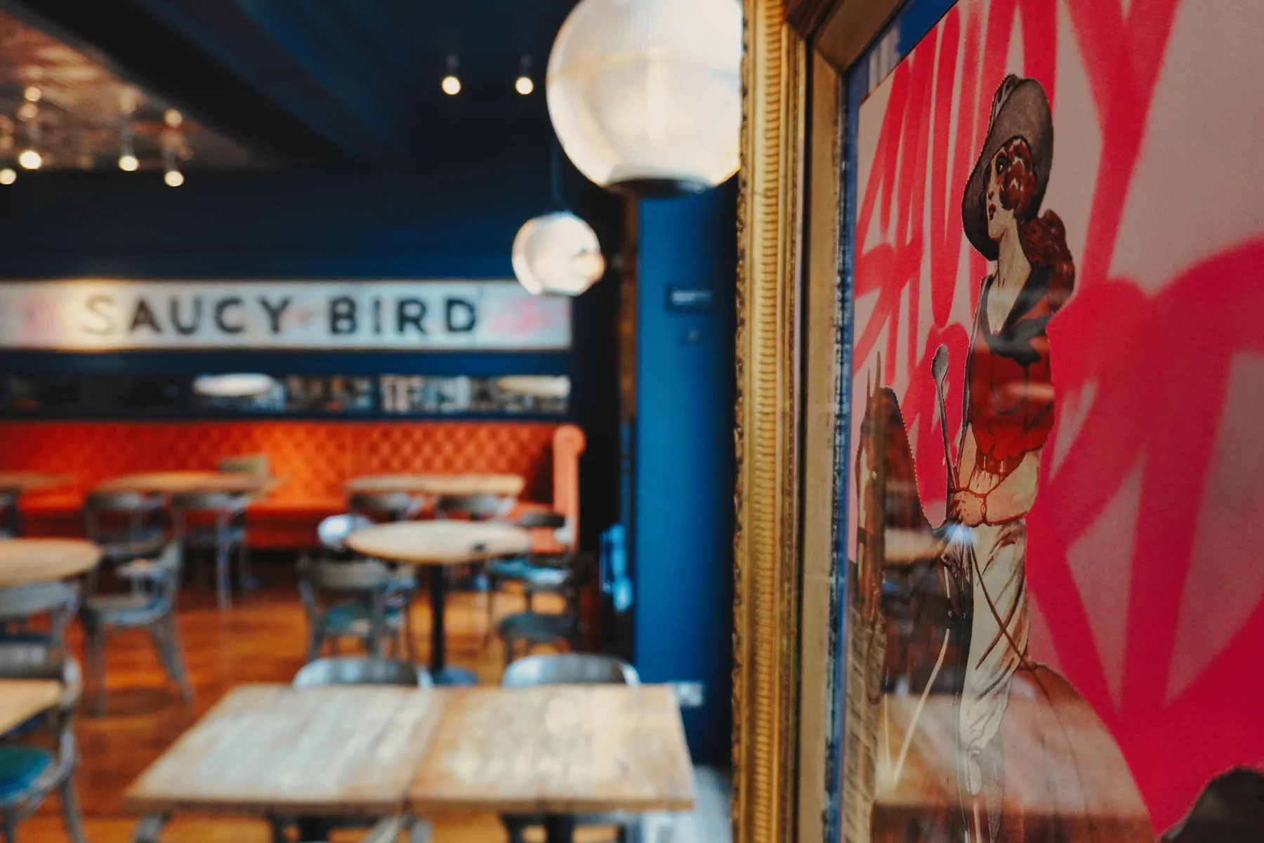 Inside Saucy Bird, with globe pendant lights, banquette seating and framed artwork