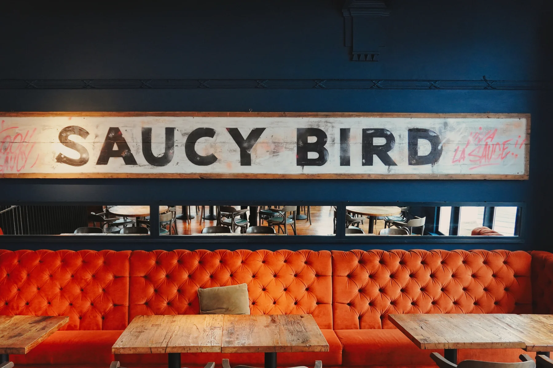 Saucy Bird sign above the orange upholstered banquette